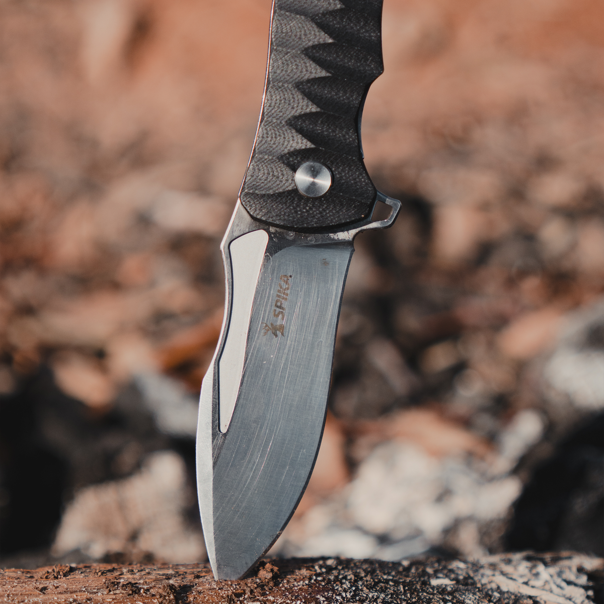 Close-up of the Spika Bushmaster Viper blade tip and Spika logo, knife standing in a log outdoors