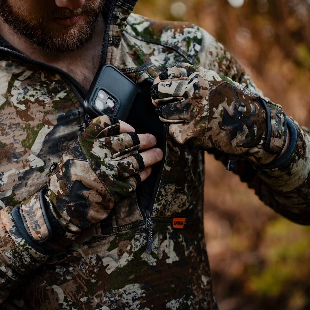 Hunter wearing Spika Precision fingerless gloves in Biarri Camo pulling a phone from a jacket