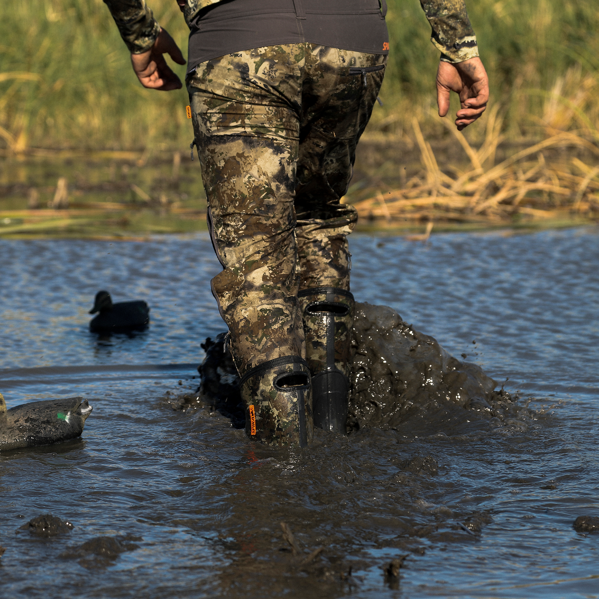 Hunter striding through mud and water in Spika Bruzer gumboots past floating duck decoys
