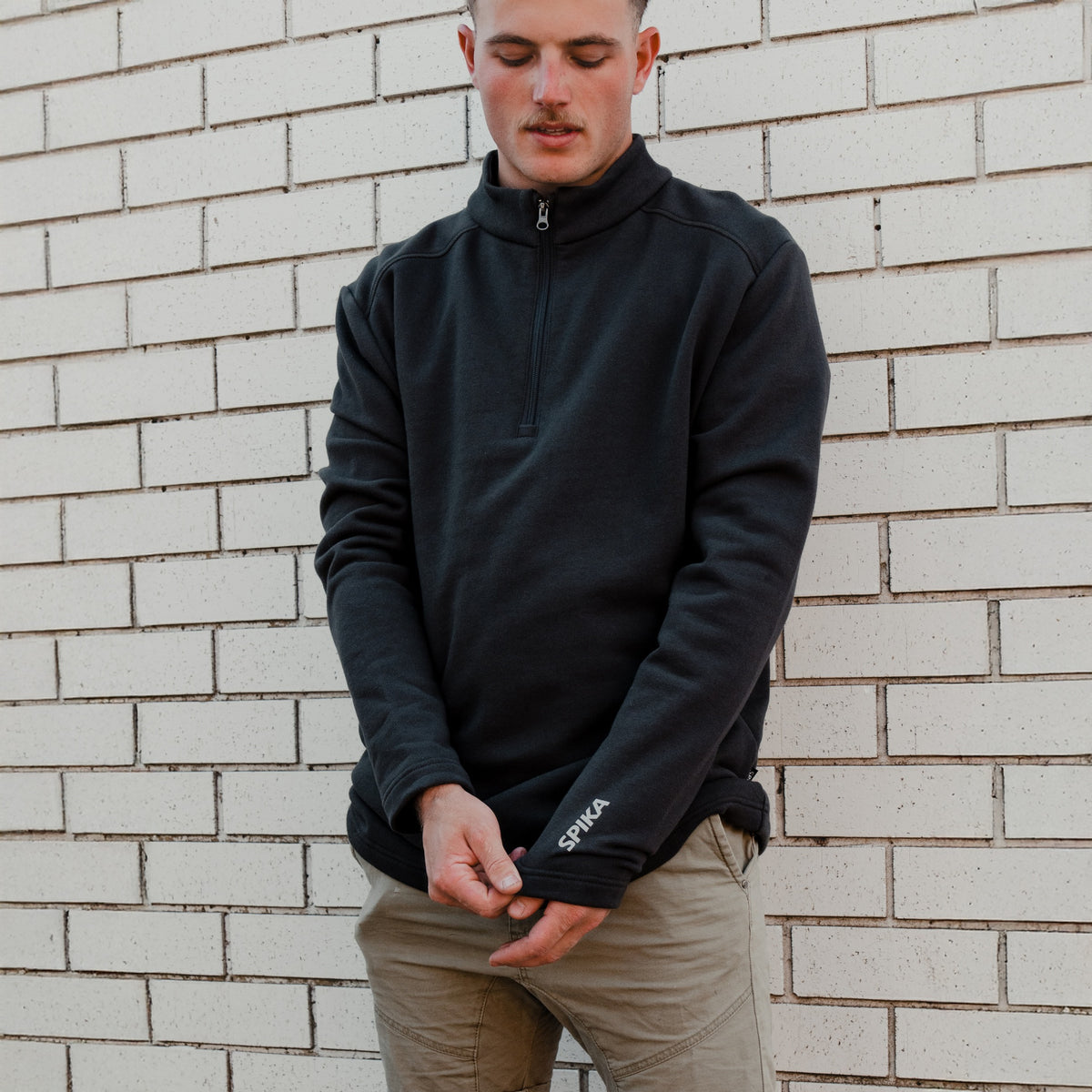 Man in the Spika GO Belay slate quarter-zip jumper adjusting the cuff, showing the SPIKA sleeve logo