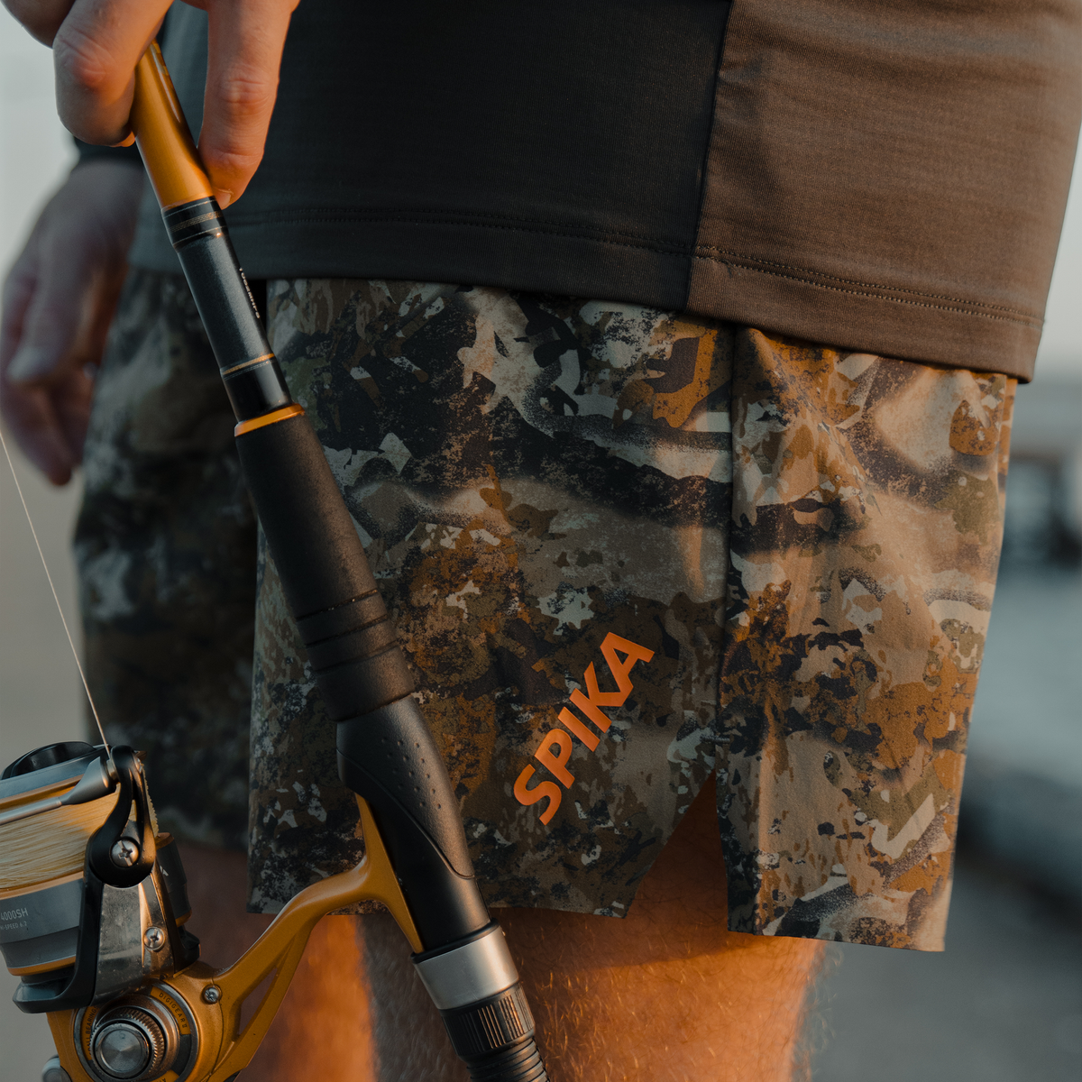 Angler wearing Spika GO Arid men's quick dry shorts in Biarri Camo, holding a fishing rod