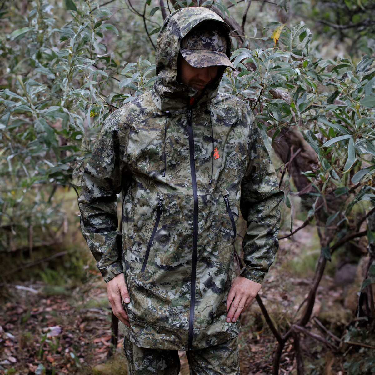 Hunter wearing the Spika Edge waterproof jacket in Biarri Camo with hood up in the bush