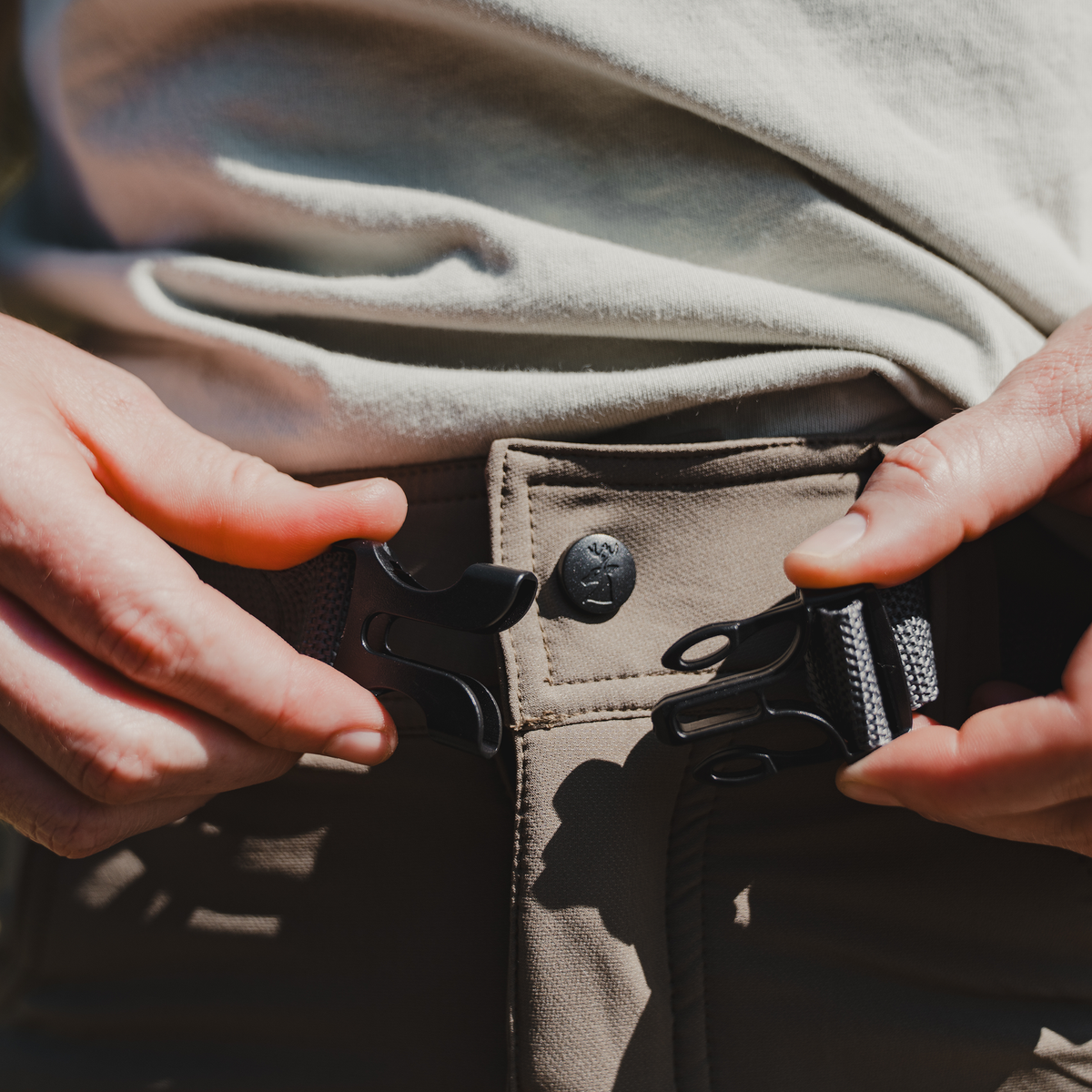 Spika Recon women's pants, hands fastening the webbing belt buckle at the waist