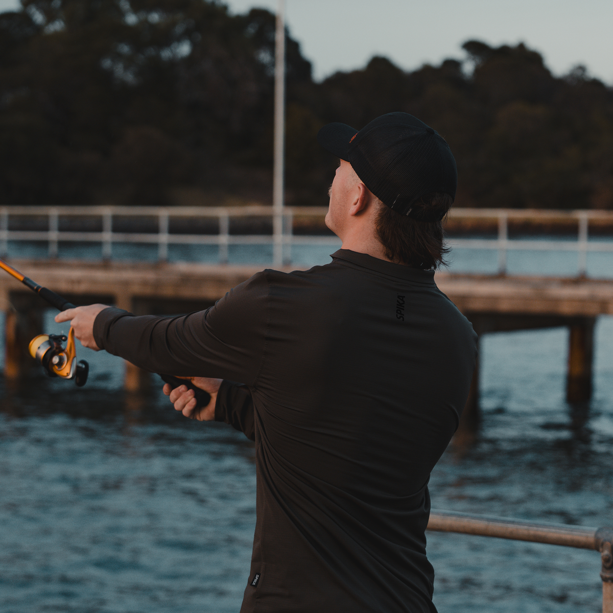 Angler casting from a jetty at dusk wearing the Spika Enduro athletic top in Olive Summit