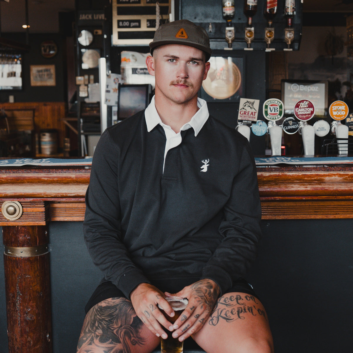 Man wearing the Spika GO Advance men's rugby jumper in slate with white collar, seated at a pub bar
