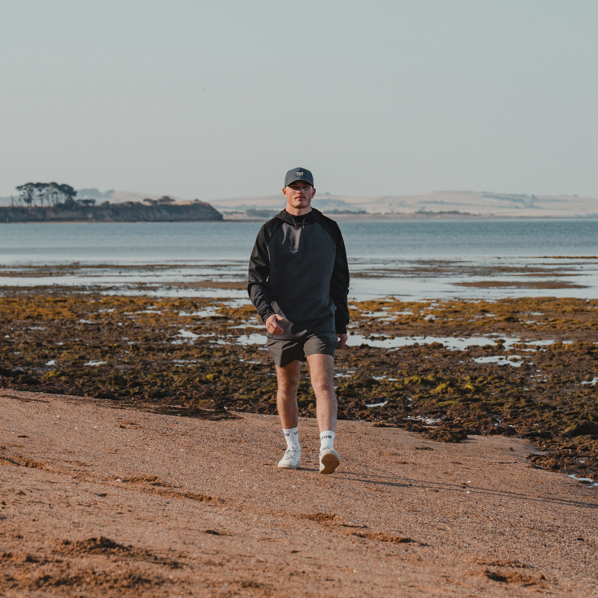 Man in a cap walking along the beach wearing the Spika GO Scuba men's slate and black hoodie