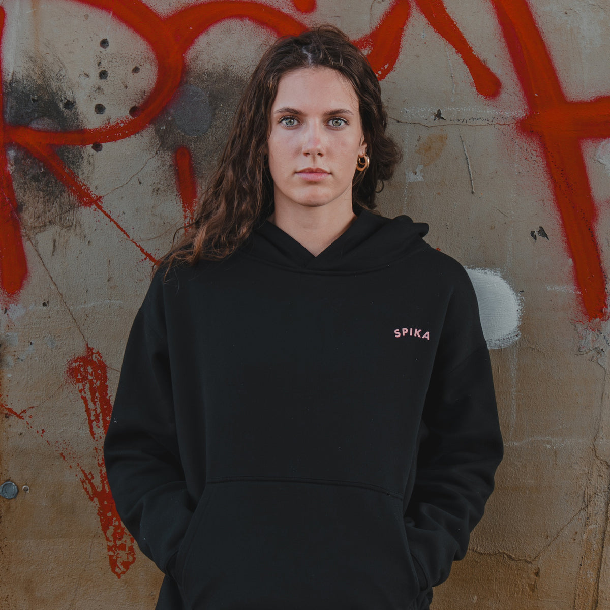 Woman wearing the Spika GO Contour women's black hoodie in front of a graffiti wall, waist-up