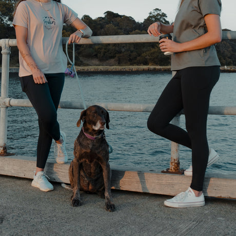 Two women with a dog leaning on a jetty railing, both wearing Spika GO Ember black leggings