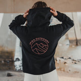 Woman pulling up the hood of the Spika GO Contour black hoodie, showing the mountain back print