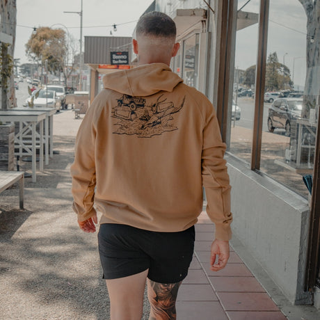 Man walking down a street in the Spika GO Deer Camp bone hoodie, showing the campsite back print