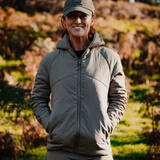 Woman wearing the Spika Aura hybrid puffer jacket in Dusky Green and a cap, smiling outdoors in bushland