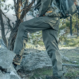 Hunter wearing Spika Scout men's pull-on pants in Olive stepping up onto a rock with a backpack