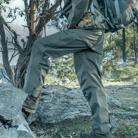 Hunter wearing Spika Scout men's pull-on pants in Olive stepping up onto a rock with a backpack