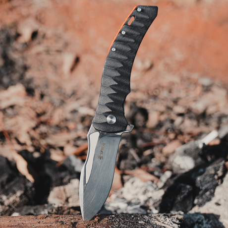 Spika Bushmaster Viper folding knife blade planted in a log outdoors with leaf litter behind