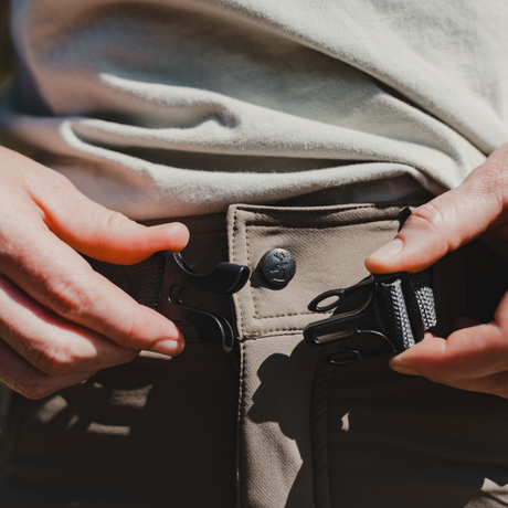 Spika Recon women's pants, hands fastening the webbing belt buckle at the waist