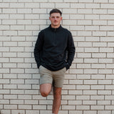 Man wearing the Spika GO Belay men's slate quarter-zip jumper with tan shorts against a brick wall