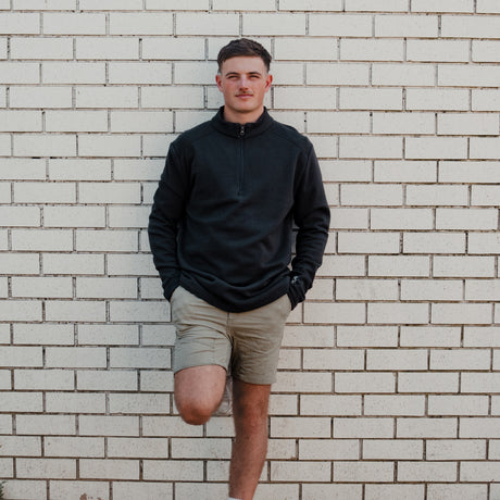 Man wearing the Spika GO Belay men's slate quarter-zip jumper with tan shorts against a brick wall
