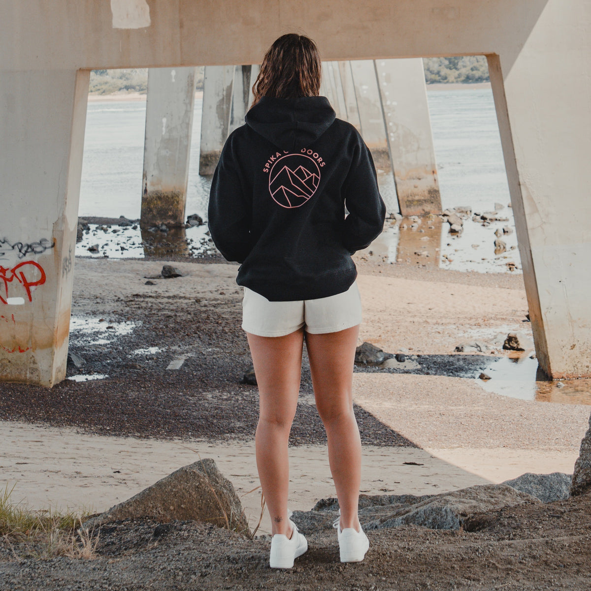 Woman in the Spika GO Contour black hoodie standing under a bridge, rear view of mountain print