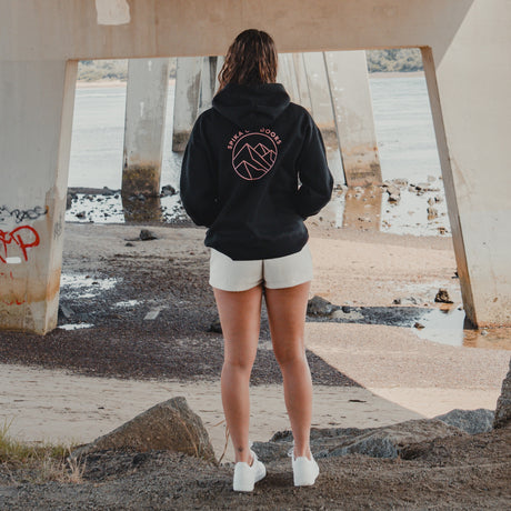Woman in the Spika GO Contour black hoodie standing under a bridge, rear view of mountain print