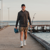 Man walking along a jetty with a tackle box and rod wearing a Spika Enduro quarter-zip top