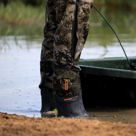 Spika Bruzer men's Biarri Camo gumboot at the water's edge beside a boat on a sandy bank