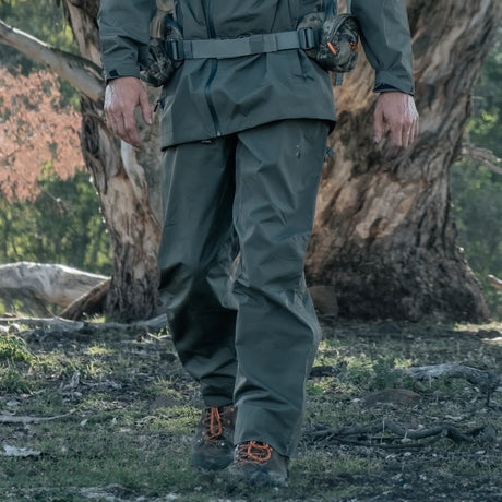 Hunter wearing Spika Scout men's pull-on pants in Olive walking through bushland past a gum tree