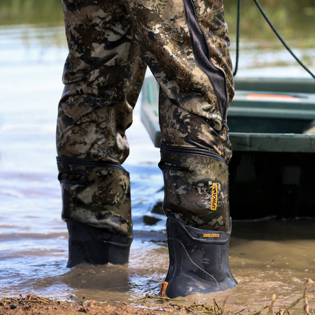 Hunter in camo waders standing in shallow water beside a boat wearing Spika Bruzer gumboots