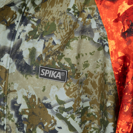 Close-up of the Spika logo badge on the chest of the Valley men's jacket in Biarri Camo/Blaze