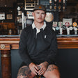 Man wearing the Spika GO Advance men's rugby jumper in slate with white collar, seated at a pub bar