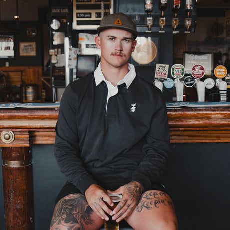 Man wearing the Spika GO Advance men's rugby jumper in slate with white collar, seated at a pub bar