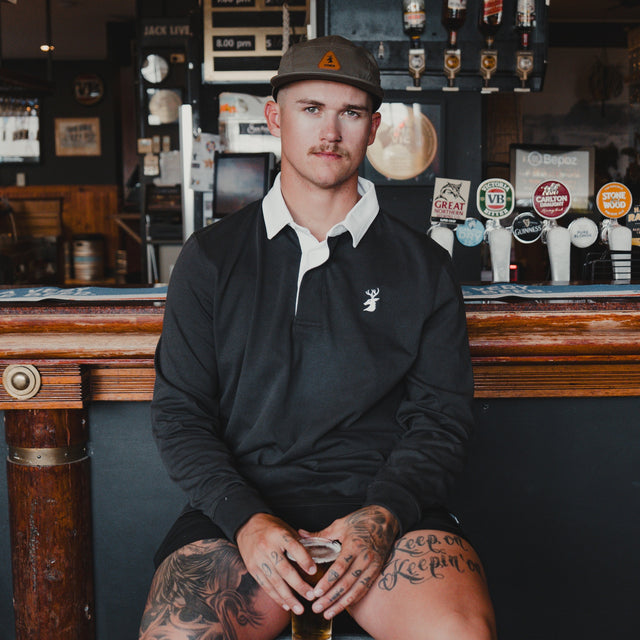Man wearing the Spika GO Advance men's rugby jumper in slate with white collar, seated at a pub bar