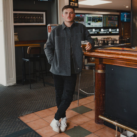 Man wearing the Spika GO Civvy slate shirt jacket with black pants, leaning on a pub bar with a beer
