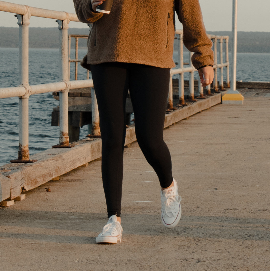 Woman in a fleece jacket walking along a jetty wearing Spika GO Ember women's black leggings