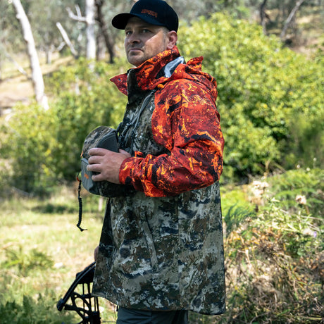 Bowhunter wearing the Spika Valley men's jacket in Biarri Camo/Blaze holding binoculars in the bush