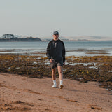 Man in a cap walking along the beach wearing the Spika GO Scuba men's slate and black hoodie