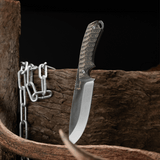 Spika Bushmaster Dogtooth knife standing blade down beside timber, antler and a steel chain