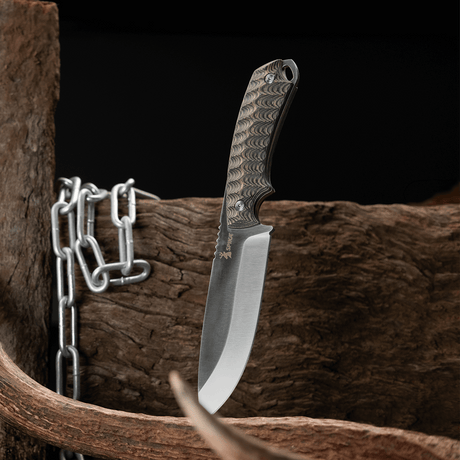 Spika Bushmaster Dogtooth knife standing blade down beside timber, antler and a steel chain