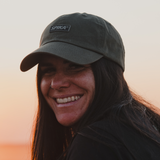 Smiling woman wearing the Spika GO Advance dad cap in Olive at sunset
