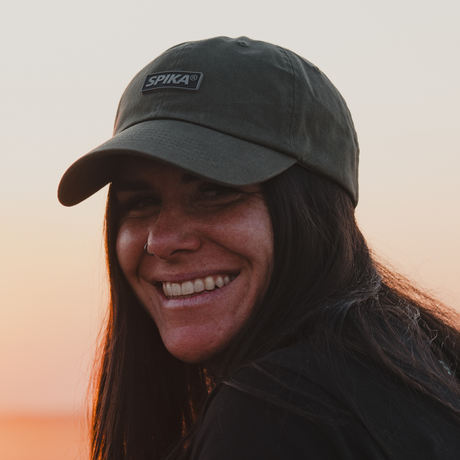 Smiling woman wearing the Spika GO Advance dad cap in Olive at sunset