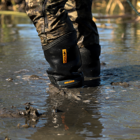 Spika Bruzer gumboot with black neoprene upper splashing through mud in a shallow wetland