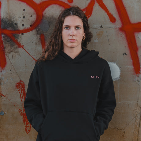Woman wearing the Spika GO Contour women's black hoodie in front of a graffiti wall, waist-up